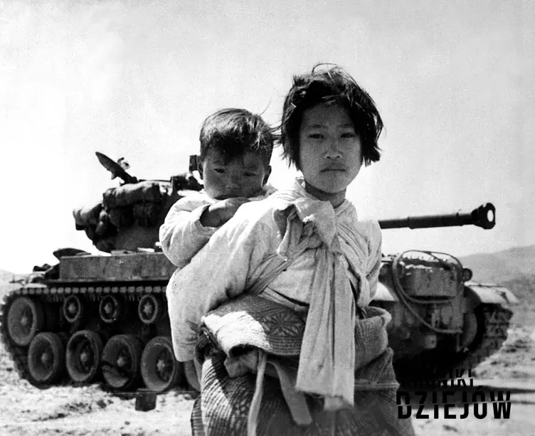 Koreanka trzyma na plecach małe dziecko na tle czołgu, jakie były przyczyny wybuchu wojny koreańskiej, skutki wojny koreańskiej